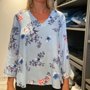 Blommig blus från Gina Tricot - Säljer en superfin blommig blus från Gina Tricot i storlek 34. Blusen är ljusblå med ett vackert blommönster i blått, rött och vitt. Den har en v-ringad hals och trekvartsärmar. Perfekt för både vardag och fest!