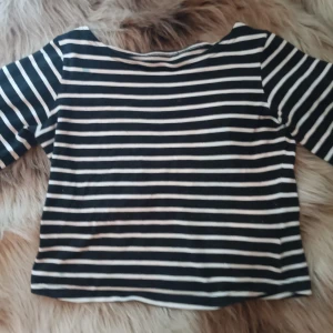 Randig topp med trekvartsärm - Säljer en snygg randig topp med trekvartsärm. Den är svart och vit med ett klassiskt randigt mönster. Perfekt för både vardag och skola!