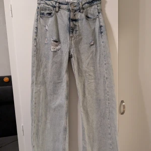 Ljusa jeans med slitningar från Denim Co. - Säljer ett par ljusa jeans från Denim Co. med coola slitningar på framsidan. De har en avslappnad passform och är perfekta för en casual look. Jeansen är i storlek 36 och har en hög midja och vida ben.
