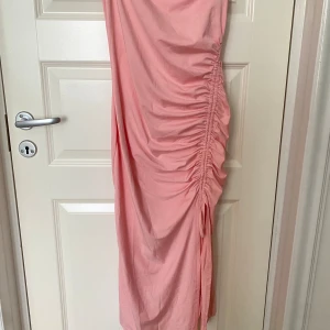Rosa klänning med rynkdetaljer - Säljer en superfin rosa klänning med rynkdetaljer på sidan. Den har smala axelband och en elegant, lång design. Perfekt för sommarens fester eller en dag på stan. Klänningen är i ett mjukt och bekvämt material.