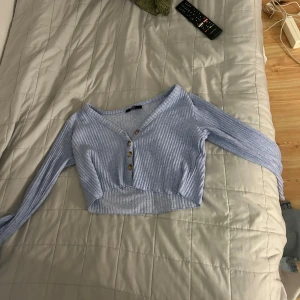 Ljusblå ribbad croppad topp från Bershka - Säljer en superfin ljusblå ribbad topp från Bershka. Den är croppad och har långa ärmar, perfekt för en casual look. Toppen har en v-ringning och tre knappar framtill. Den är i storlek XS och är i bra skick. Perfekt för vår och sommar! en liten fläck