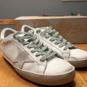 Golden Goose skor - Snygga vita sneakers från Golden Goose med en ikonisk stjärndetalj i mocka på sidan. Skorna har grå snörning och en bekväm passform. Perfekta för en stilren look.