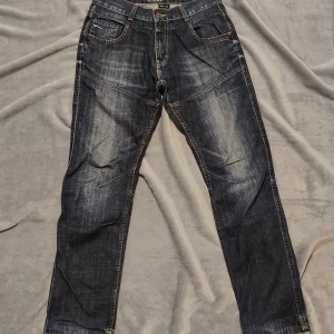 Mörkblå jeans från Grant - Snygga mörkblå jeans från Grant med klassisk femficksdesign och kontrastsömmar. Jeansen har en rak passform och är perfekta för en avslappnad stil. De har en knappgylf och bälteshällor för extra komfort.