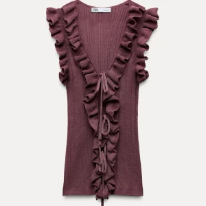 Stickad vinröd volangtopp från Zara - SLUTSÅLD ÖVERALLT!.Aldrig använd. Snygg vinröd topp/blus från Zara med volangdetaljer längs ärmarna och framsidan. Den har en ribbad struktur och knytning framtill.