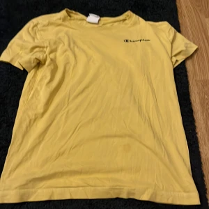 Gul t-shirt från Champion - Säljer en gul t-shirt från Champion i storlek medium. Den har korta ärmar och en klassisk passform med Champion-loggan på bröstet. Perfekt för en avslappnad stil.