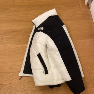 Vit och svart pufferjacka från The North Face - Säljer en snygg vit och svart pufferjacka från The North Face. Jackan har en dragkedja framtill och är långärmad. Perfekt för kyligare dagar med sin quiltade design.