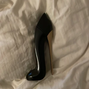 Svart högklackad parfymflaska - Snygg parfymflaska formad som en högklackad sko i svart med en elegant guldklack. Perfekt för den som vill ha en unik och stilren design på sin parfymflaska. Flaskan har en modern och lyxig känsla som passar perfekt på sminkbordet.