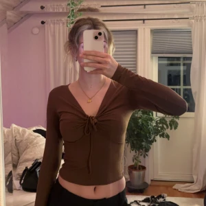 Brun långärmad topp från Bik Bok - Säljer en brun långärmad topp från Bik Bok i storlek XS. Toppen har en v-ringad design med knytning framtill och är croppad. Perfekt som fest topp✨✨Frakt ingår i priset 