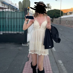 Krämfärgad klänning med spetsdetaljer - Charmig krämfärgad klänning med spetsdetaljer och öppen rygg. Klänningen har en v-ringad design och knytband i ryggen för en justerbar passform. Perfekt för varma sommardagar. Storleken är en M men passar lika bra för en som har S! 