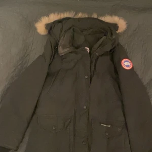 Svart parkajacka från Canada Goose - Säljer en svart parkajacka från Canada Goose med pälsdetaljer på huvan. Jackan har en klassisk design med lång ärm och praktiska fickor. Perfekt för kalla vinterdagar. Den har ett par år på nacken för att det var mammas gamla men hon tänkte då slänga den så kanske någon vill köpa den för en billig peng istället 