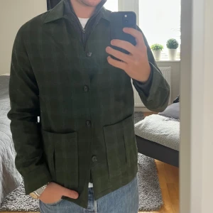 Grön rutig overshirt - (Helt ny aldrig använd).Snygg grön rutig overshirt från John Henric. Jackan har fickor med knappar framtill. Perfekt för lager-på-lager-stil.