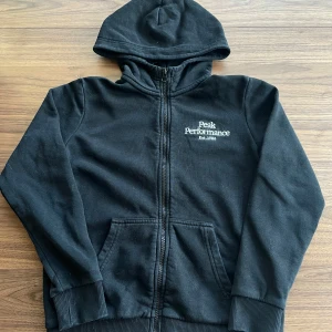 Svart zip hoodie från Peak Performance - Säljer en svart zip hoodie från Peak Performance med dragkedja och huva. Tröjan är använd men fortfarande i bra skick. Storlek 150 