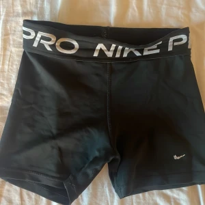 Svarta träningsshorts från Nike - Säljer ett par svarta träningsshorts från Nike Pro med elastisk midja och logga. Storlek M, jag brukar ha storlek xs/s i kläder och de sitter tajt på mig.