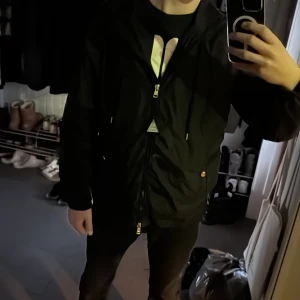 Svart jacka från Moncler - Snygg svart jacka från Moncler med dragkedja och huva. Jackan har en normal passform och är perfekt för höst- och vårsäsongen. Den har Monclers logotyp på ärmen och praktiska fickor med knappar. Köpt 5000 på Plick. 