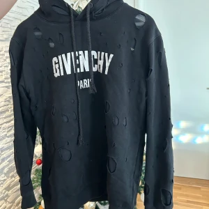 Svart hoodie från Givenchy - Snygg svart hoodie från Givenchy med vit logga på bröstet. Hoodien har en unik design med slitna detaljer och dragsko i huvan. Perfekt för en trendig och avslappnad stil.