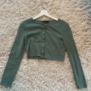 Grön kofta från Zara - Säljer en stilren, nästan helt oanvänd grön kofta från Zara. Den har långa ärmar och knappar framtill. Perfekt för lager-på-lager och passar till många olika outfits. 