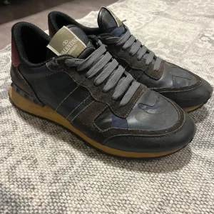 Valentino sneakers i svart och grått - Snygga Valentino sneakers i svart och grått med snörning och en robust sula. Perfekta för en stilren look med en touch av lyx.