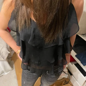 Svart ärmlös topp med volanger - Snygg svart ärmlös topp med volanger. Perfekt för en kväll ute eller en speciell tillställning. Toppen har en luftig och lätt design som ger en elegant look. Skriv för fler bilder eller om ni har frågor💛