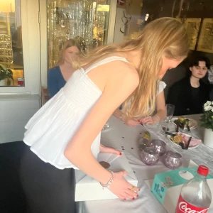 Vit ärmlös blus - Snygg vit ärmlös blus med smockdetaljer och volang nedtill. Perfekt för sommarens festligheter.