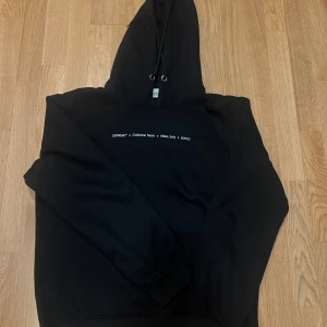 Svart hoodie från Off-White - Säljer en svart hoodie från Off-White med tryck på bröstet och en stor grafisk design på ryggen i grönt och vitt. Hoodien har en justerbar huva med dragsko och en praktisk magficka. Perfekt för en stilren och modern look. Storlek L men passar M perfekt