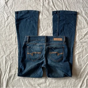 Blå bootcut jeans - Snygga blå bootcut jeans med klassisk femficksdesign och knappgylf. Tillverkade i en bomullsblandning med lite stretch för extra komfort. Perfekta för en avslappnad stil.