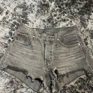 Grå jeansshorts från Levi's - Säljer ett par grå Levi's 501 jeansshorts med hög midja och slitna kanter. Perfekta för en avslappnad stil. Klassisk design med fem fickor och knappgylf.