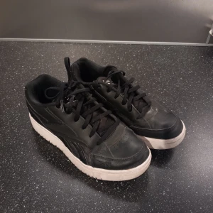 Svarta sneakers från Reebok - Säljer ett par svarta Reebok sneakers med vit sula och klassisk snörning. Skorna har en stilren design med Reebok-loggan på hälen. Dem har använts sparsamt. 