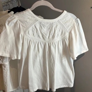 Vit blus från Zara - Säljer en söt vit blus från Zara med vackra broderade detaljer på framsidan. Blusen har korta ärmar och en rund halsringning, perfekt för en stilren look. Passar utmärkt till både jeans och kjol. Storlek 11-12 år men passar mig som är xs/s.