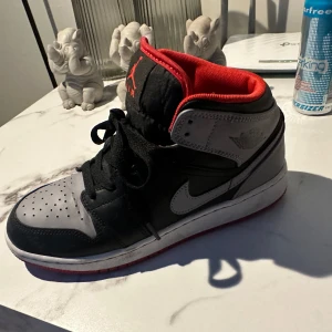 Nike Air Jordan sneakers i svart och grått - Snygga Nike Air Jordan sneakers i svart och grått med röda detaljer. Skorna har en klassisk design med snörning och en bekväm passform. Perfekta för en stilren look.