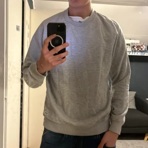 Grå sweatshirt från lager 157 - Säljer en stilren grå sweatshirt från lager 157 i storlek M. Tröjan har en klassisk rund hals och ribbade muddar vid ärmslut och nederkant. Perfekt för en avslappnad look.