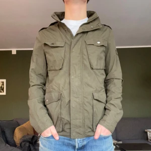 Olivgrön Fieldjacka från Woolrich - Säljer en asfet Fieldjacket från Woolrich med flera praktiska fickor och knappar. Jackan har en klassisk design med hög krage och är perfekt för vårsäsongen som kommer. Hör av er vid frågor!👍