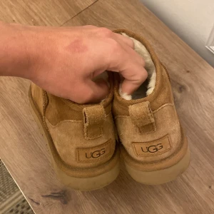 Bruna UGG boots med foder - Säljer ett par bruna UGG boots i mocka med mjukt foder. De har en rund tå och en robust sula för extra komfort. Perfekta för kyligare väder.