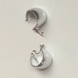 Silvriga örhängen med vågig kant - Snygga silvriga örhängen med en unik vågig kantdesign. Perfekta för att ge en stilren touch till din outfit. De har en enkel krok för enkel användning.