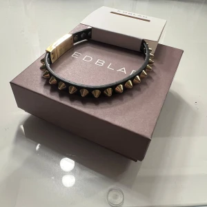 Svart armband med guldnitar från Edblad - Snyggt svart läderarmband från Edblad dekorerat med guldnitar. Magnetspänne, lätt att få på och av själv. Helt nytt, aldrig använt endast testat.