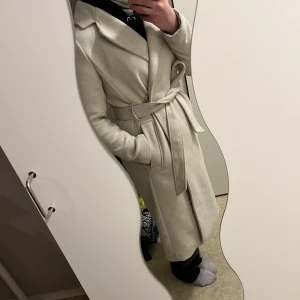 Beige kappa med slits baktill - Fin beige kappa från H&M säljes då den inte kommer till användning längre, endast använd en höst och vinter. En av knapparna i midjan har börjat lossna men går nog att sy fast eller användas utan knapp. Kan finnas några småfläckar som borde gå bort i tvätten. Storlek 36, nypris 5-600kr mitt pris: 200kr