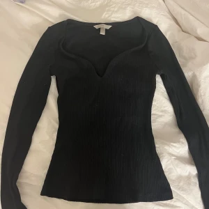 Svart ribbad tröja - Säljer en stilren svart ribbad tröja med lång ärm och v-ringning. Perfekt för en elegant och enkel look. Passar bra till både jeans och kjol.
