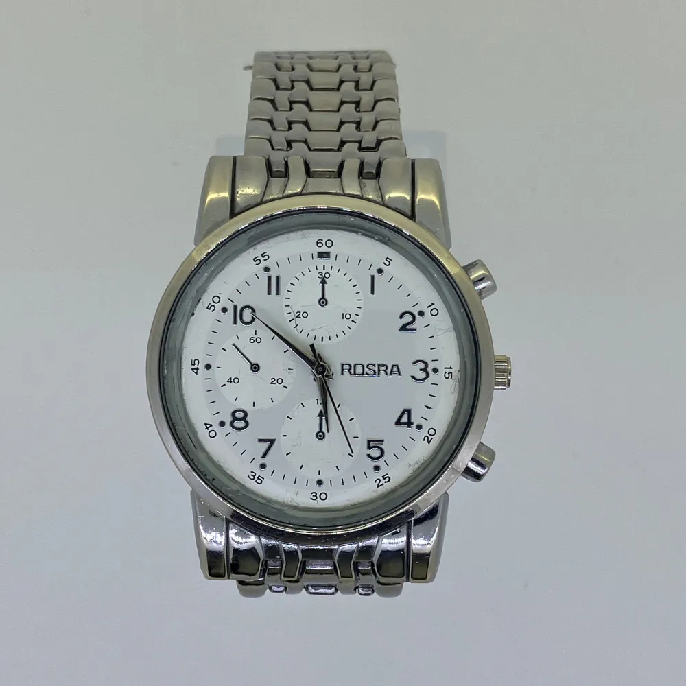 Stilren silverfärgad klocka från Rosra med vit urtavla och tydliga svarta siffror. Klockan har en förkortad metallarmband och flera små dekorativa urtavlor för extra snygg look. Quartz batteri, fungerar perfekt.. Asusteet.