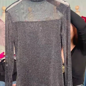 Glittrig svart långärmad topp - Snygg och glittrig svart topp med lång ärm och transparenta detaljer vid axlarna. Perfekt för en kväll ute eller festliga tillfällen. Toppen har en elegant och modern design som drar blickarna till sig.