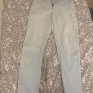 Ljusblå chinos från Tommy Hilfiger - Snygga ljusblå chinos från Tommy Hilfiger i slim fit. Byxorna har en klassisk design med knappar bak och bälteshällor. Perfekta för en stilren look.