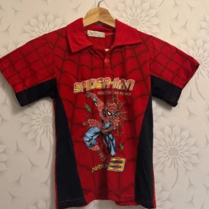 Röd och svart Spiderman t-shirt - Cool röd och svart Spiderman t-shirt med korta ärmar och ett stort tryck av Spiderman på framsidan. T-shirten har ett spindelnätsmönster och en klassisk krage. Perfekt för fans av superhjältar!