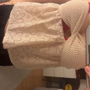 Beige topp från Shein - Säljer en söt beige topp från Shein med broderade blommor och en ribbad överdel. Toppen har en omlott-design och är perfekt för sommardagar. Tillverkad i polyester.