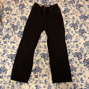 Svarta Levi's Ribcage Straight jeans - Snygga svarta Levi's Ribcage Straight jeans med hög midja och klassisk knappgylf. Perfekta för en stilren look med raka ben och tidlös design.