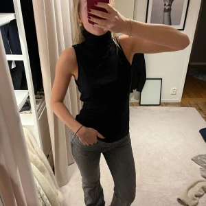 Svart ärmlös polotopp - Snygg svart ärmlös polotopp med hög krage. Perfekt för en stilren look och kan enkelt matchas med olika outfits.