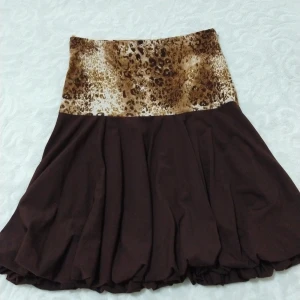 Brun kjol med leopardmönster från Lamara - Snygg brun kjol från Lamara med leopardmönstrad midja. Kjolen har en flödande design som ger en fin rörelse. Perfekt för att lägga till lite djurmönster i garderoben.