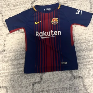 FC Barcelona fotbollströja med Messi 10 - Snygg FC Barcelona tröja från Nike med Messi 10 på ryggen. Tröjan är blå med röda ränder och har korta ärmar. Perfekt för fotbollsträningar