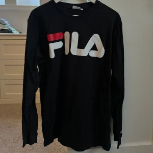 Svart långärmad tröja från FILA - Snygg svart långärmad tröja från FILA med stort logotryck i vitt och rött på bröstet. Perfekt för en avslappnad stil.
