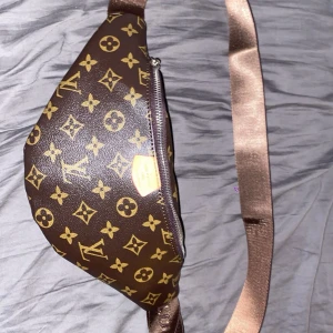 Brun midjeväska med monogram - Snygg brun midjeväska med klassiskt monogrammönster och justerbart band. Perfekt för att bära dina nödvändigheter med stil. Väskan har en praktisk dragkedja för säker förvaring.