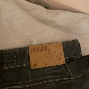 Svarta jeans från Fishbone - Snygga svarta jeans från Fishbone med coola sömmar och detaljer på bakfickorna. De har en klassisk. Märkeslappen sitter på baksidan av midjan. Dem är i storlek 30/32 och är straight leg och ger en baggy look! inte så användna men lite slitna längst ner.