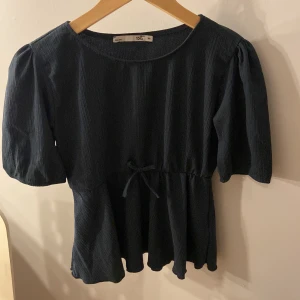 Mörkblå/mörkgrön topp med knytband - Säljer en stilren mörkblå topp från SET med knytband i midjan. Toppen har trekvartsärmar och en rund halsringning. Perfekt för en avslappnad men ändå elegant look. Storlek 160 min skulle passar även xs o s❤️