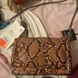 Ormmönstrad axelväska - Snygg axelväska med ormmönster i bruna och svarta toner. Väskan har en justerbar axelrem och en praktisk storlek för vardagsbruk. Perfekt för att ge din outfit en trendig touch.